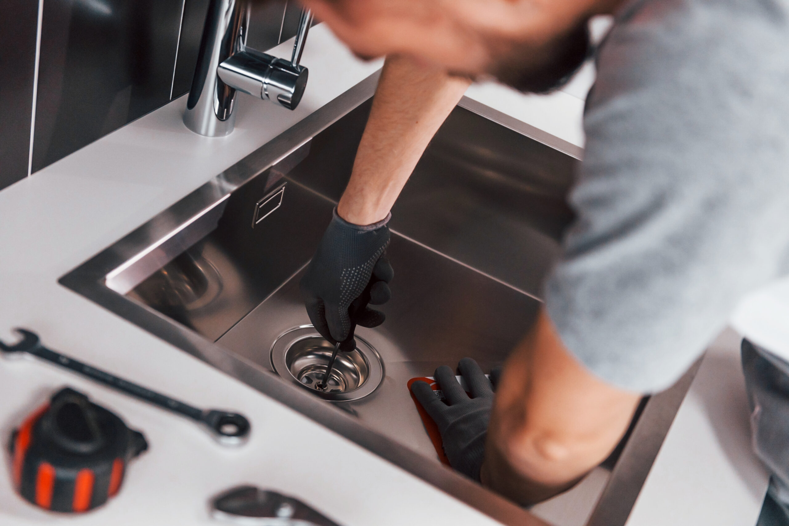 young professional plumber in grey uniform working on the kitchen