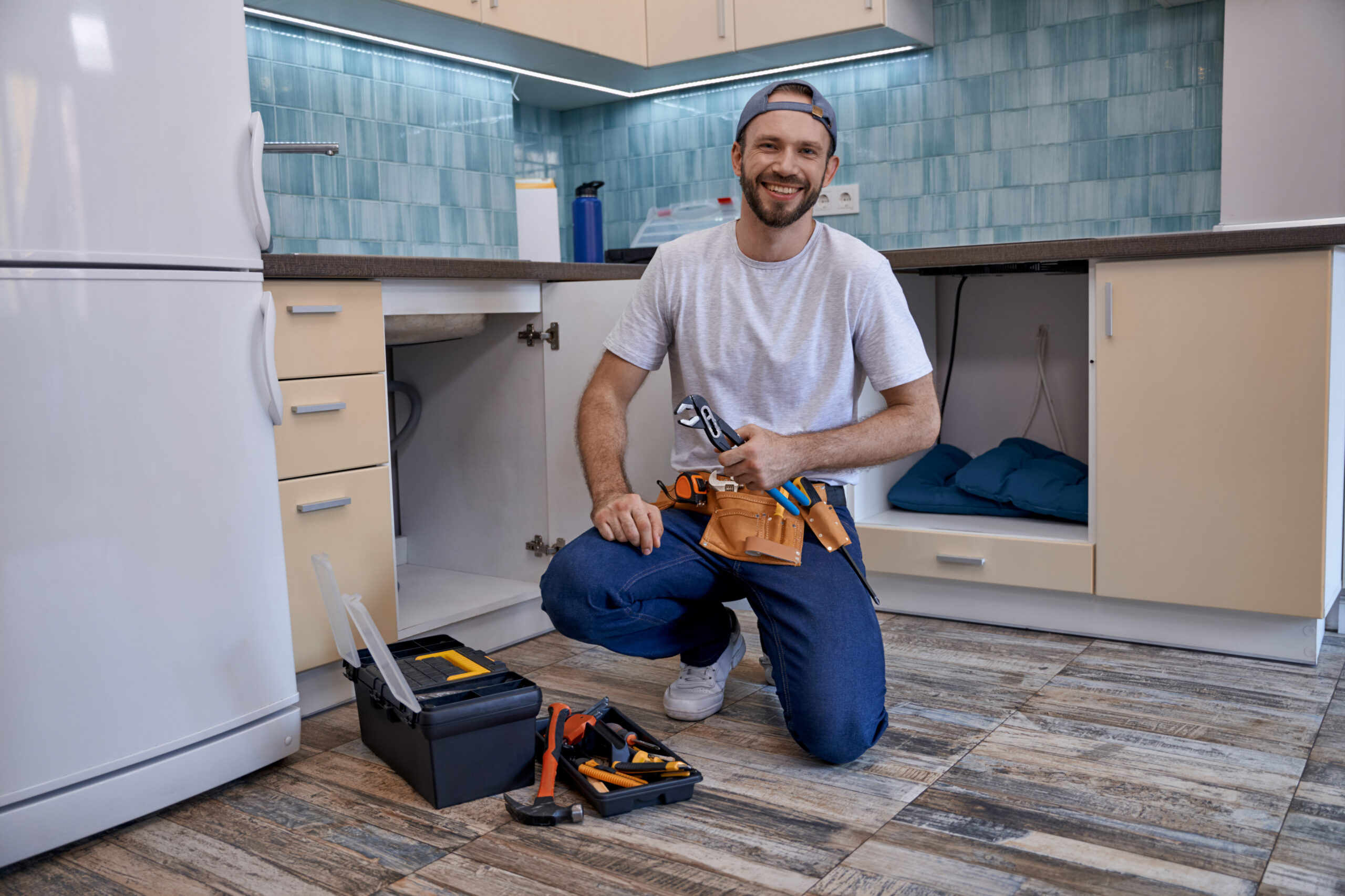 handsome caucasian male plumber sitting next to open kitchen drawer